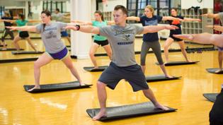 A group of male and female students working out in the wood floored exercise studio